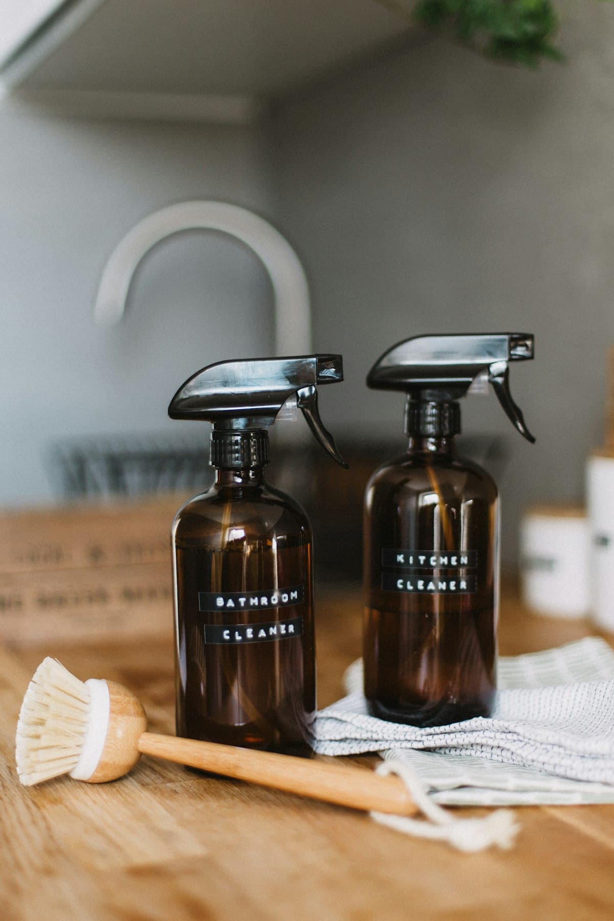 Labelled bathroom and kitchen cleaner bottles with a wooden dish brush on a counter